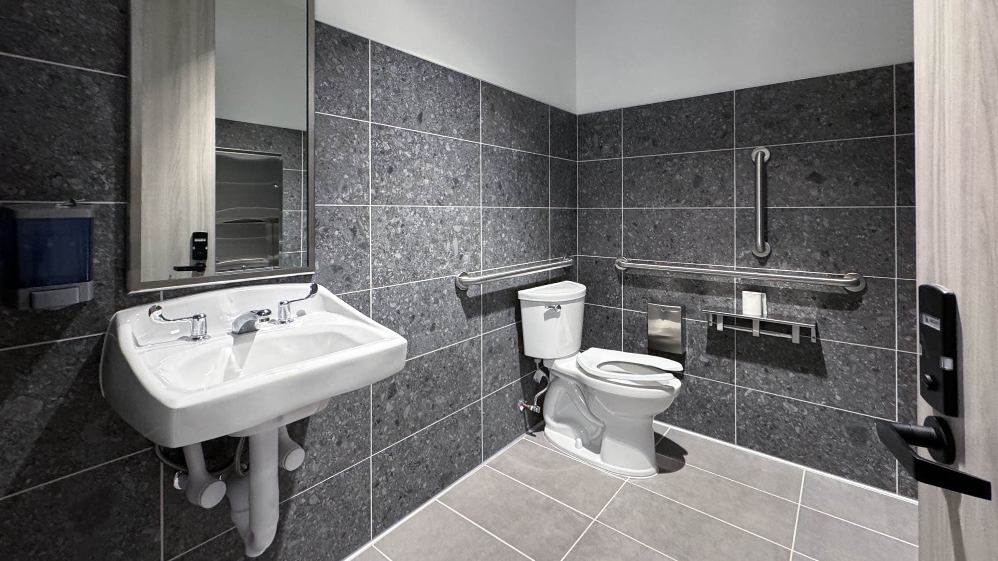 Accessible commercial bathroom with sink, toilet, and safety grab bars.