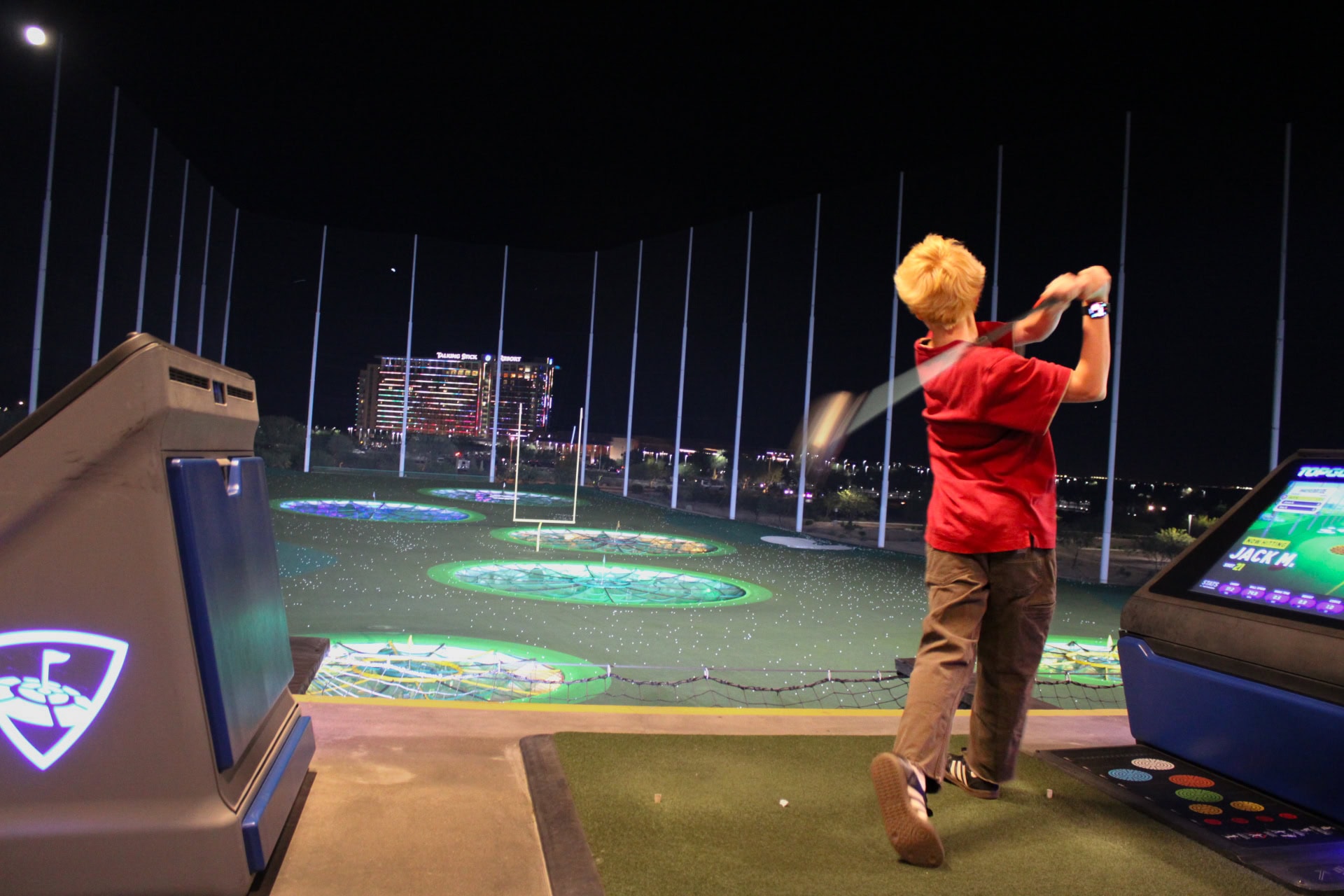 Topgolf Scottsdale at night with a young golfer swinging a club.