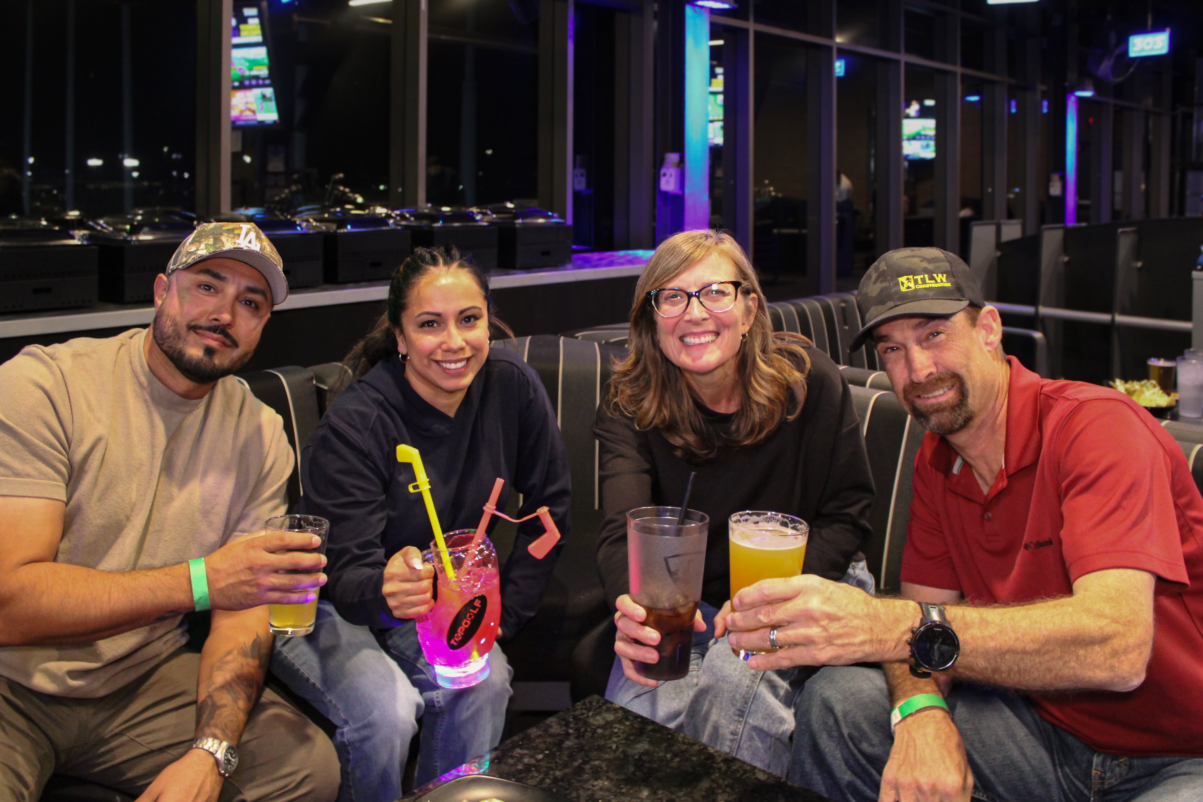 Group of four smiling people enjoying drinks at Topgolf Scottsdale during TLW Construction event.